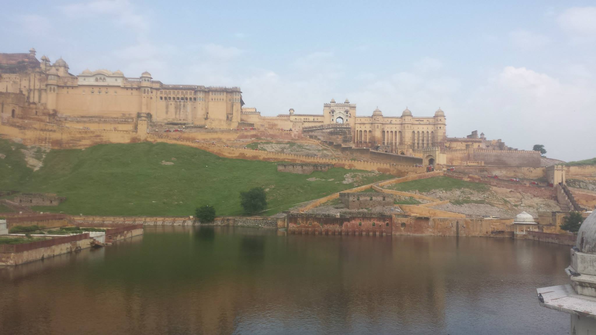 Amber Fort rising above Maota Lake — honey-colored sandstone on a forested hill